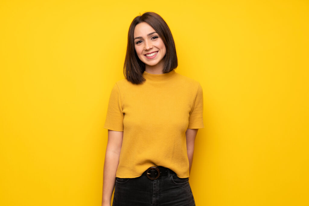 Young woman over yellow wall smiling